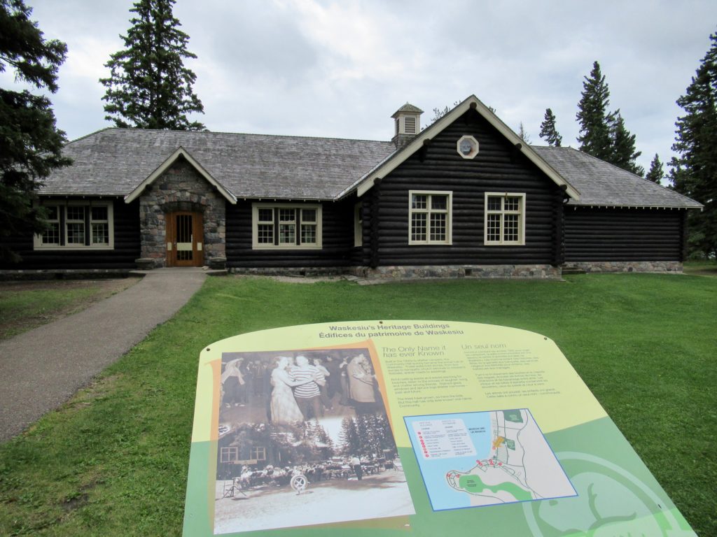 Overview of historic log community hall and an interpretive sign in Prince Albert National Park