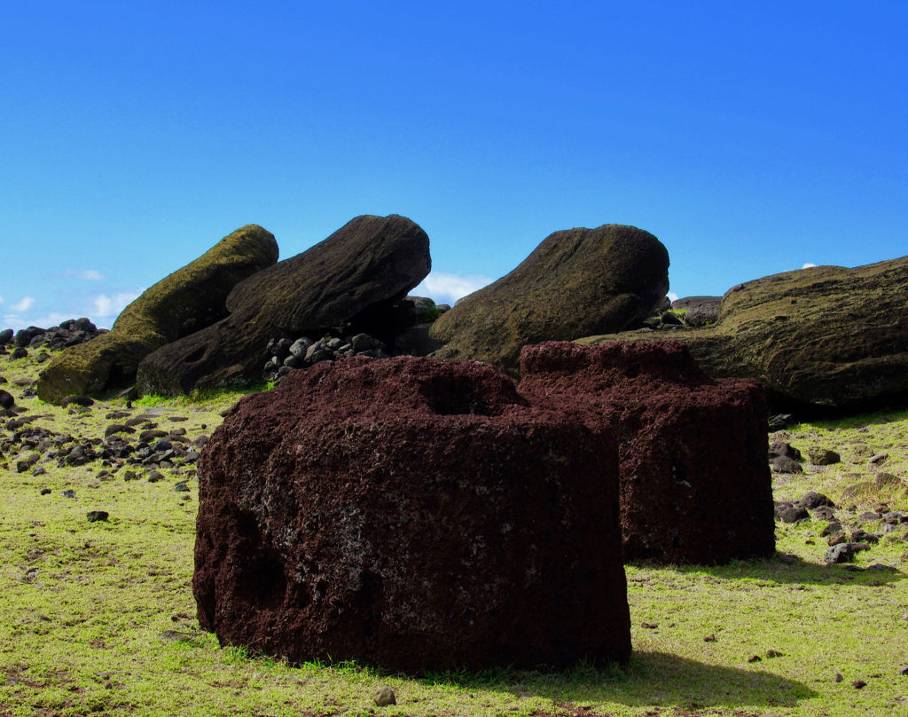 Carved round red scoria stone topknots lying in front of fallen moai on Easter Island
