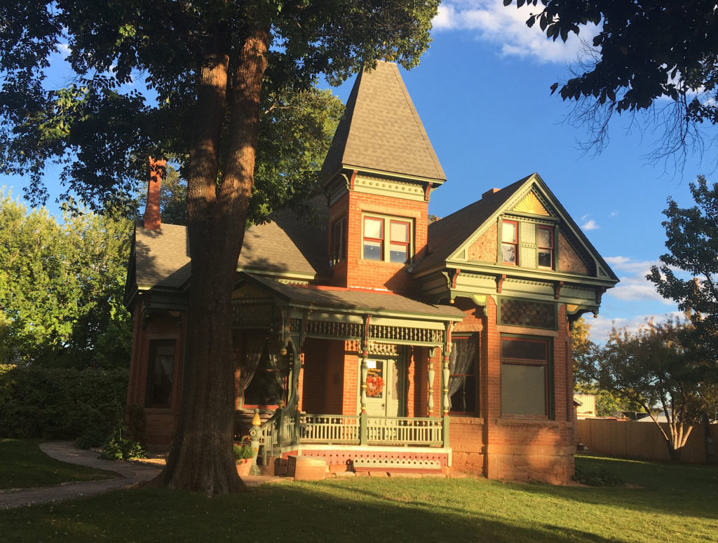 Ornate historic brick home in evening light with blue sky, green grass and tall trees.