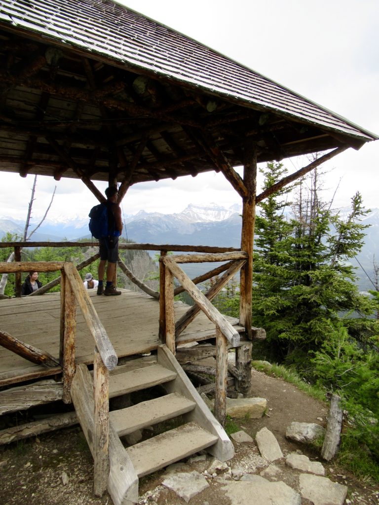 Backpacker standing in historic wooden gazebo overlooking a treed valley and distant mountains