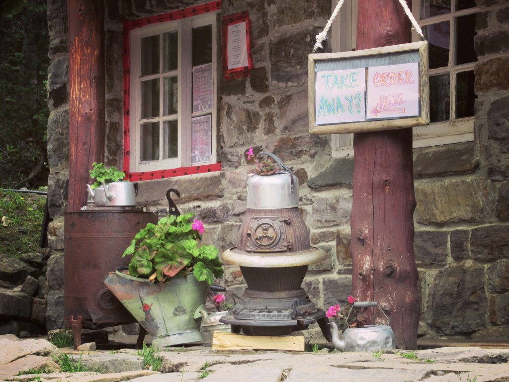 Old stone teahouse with flower-filled kettles and red log posts