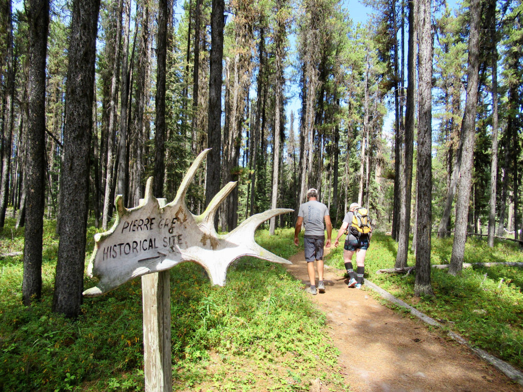 Two people hiking on trail beyond  moose antler sign reading Pierre Grey's Historical Site.