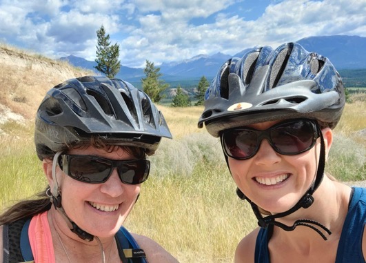 Two women wearing bicycle helmets smiling at camera.