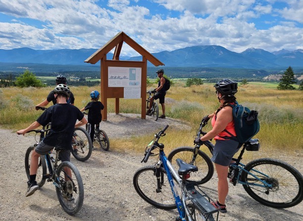 Three adults and two kids on bikes look at trail map