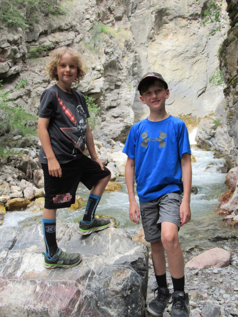 Two boys in t-shirts and shorts posing on a rock beside a creek in a canyon.