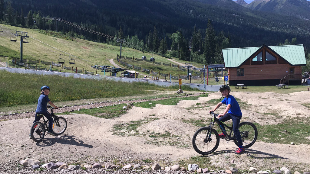 Two boys in t-shirts and long pant on bikes in dirt bike park
