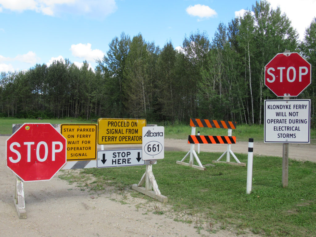 Two large stop signs and several more signs at approach to ferry crossing.