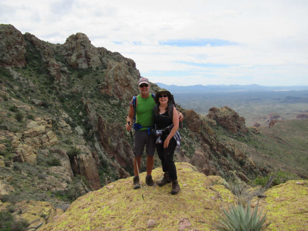 Man and woman posing for picture on lichen-covered rock on mountain slope.