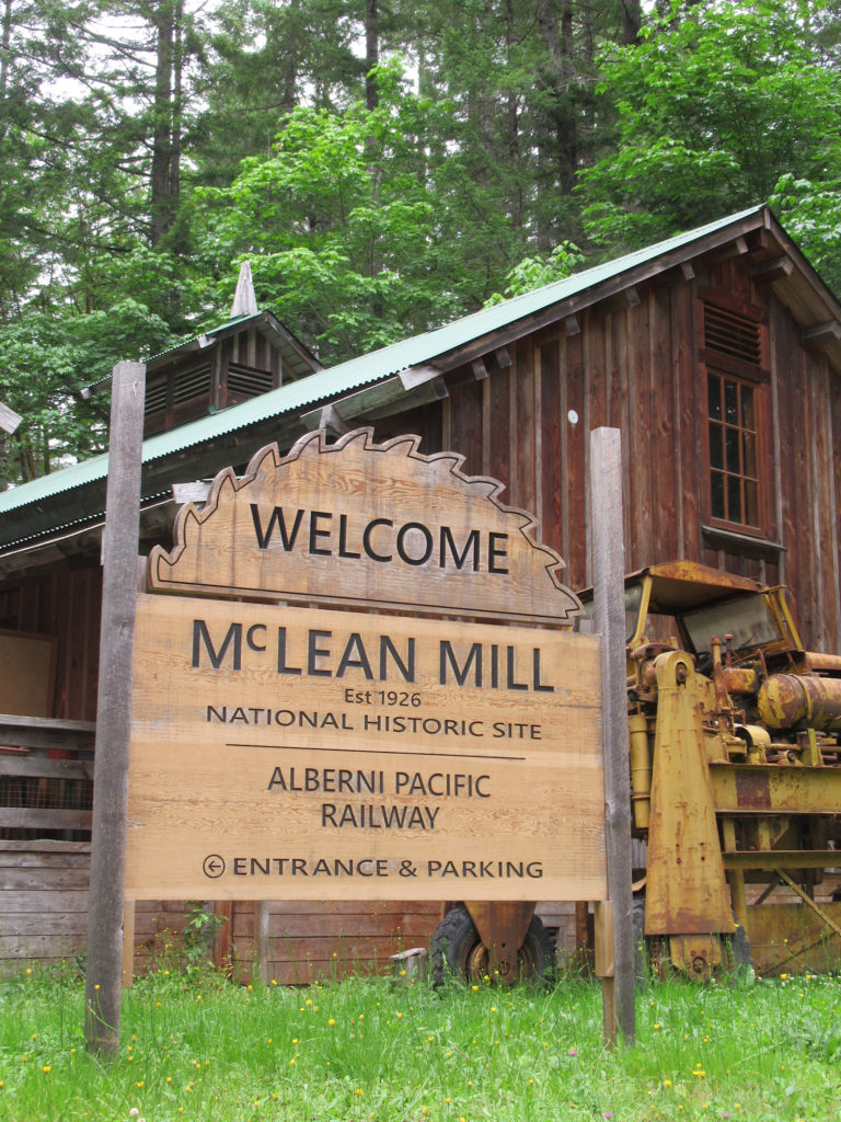 Wooden sign in shop of saw blade with words: Welcome McLean National Historic Site and Alberni Pacific Railway etched on it. 