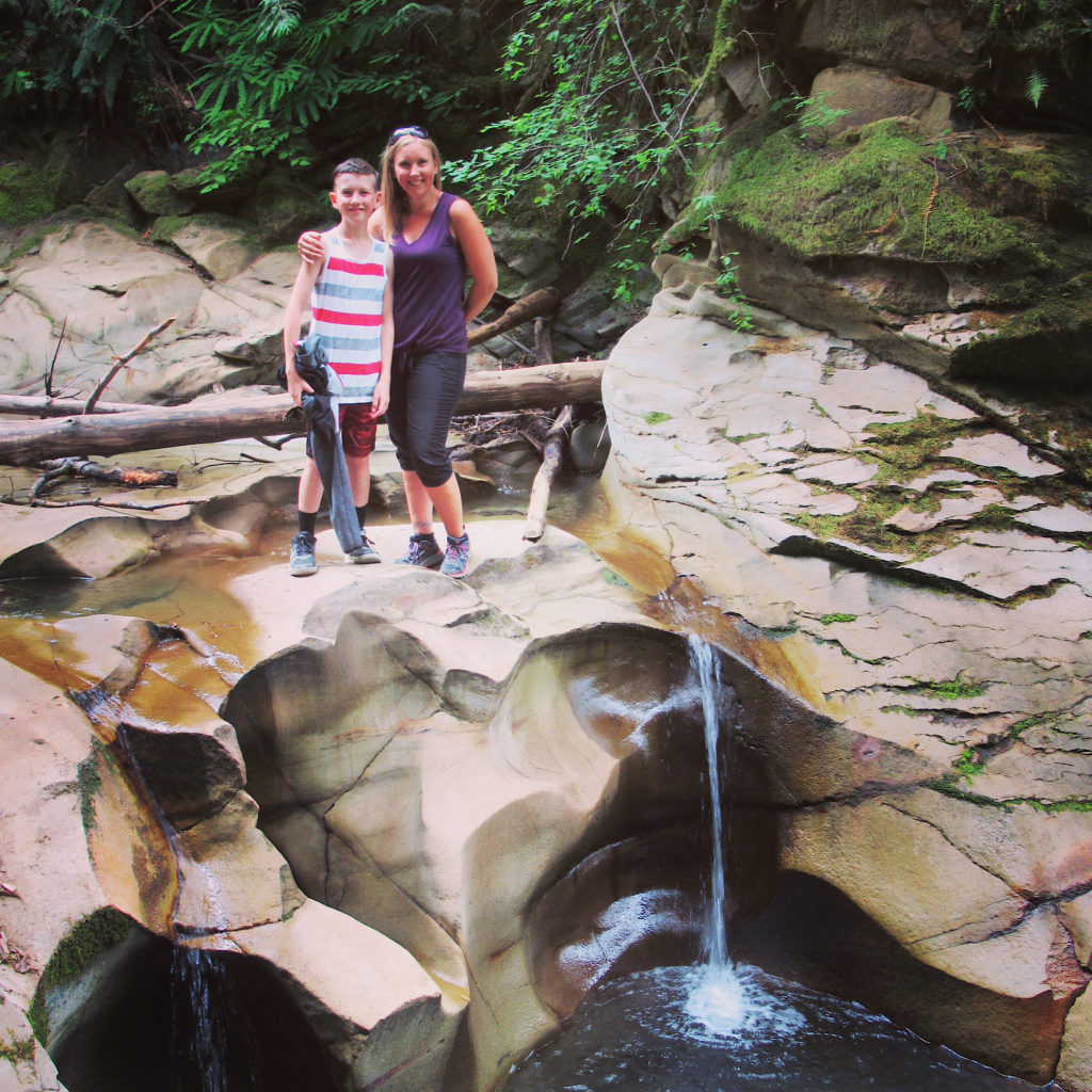 Woman and boy standing beside small waterfall and carved rock pool.