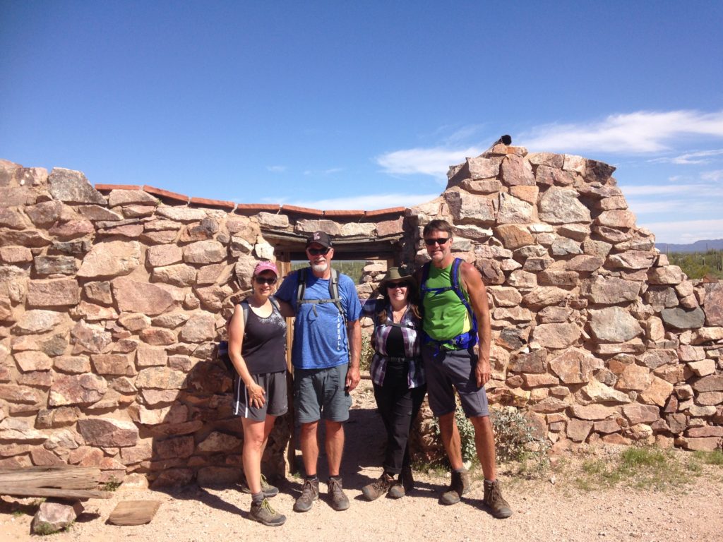 Two women and two men standing in front of an old stone building wall.