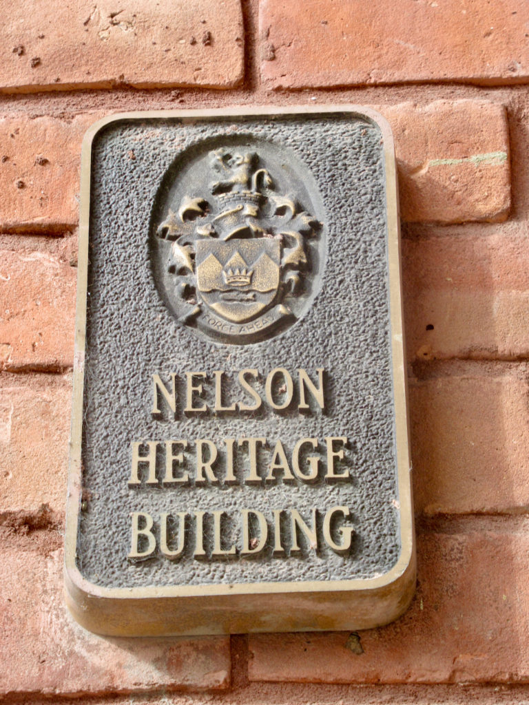 Brass plaque on red brick wall reads: Nelson Heritage Building
