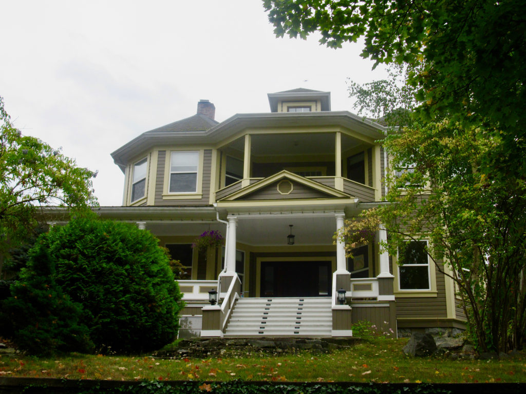 Historic home painted taupe with pale yellow trim has a large verandah and wide stairs