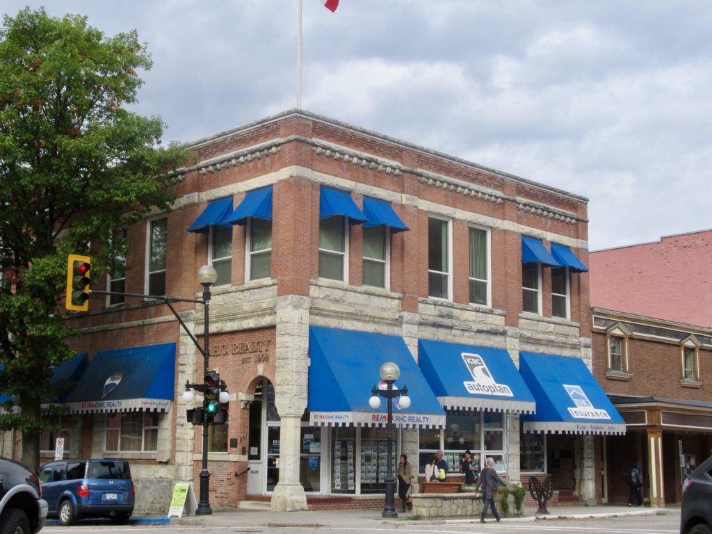 Red brick and grey stone corner building with bright blue awnings on windows.