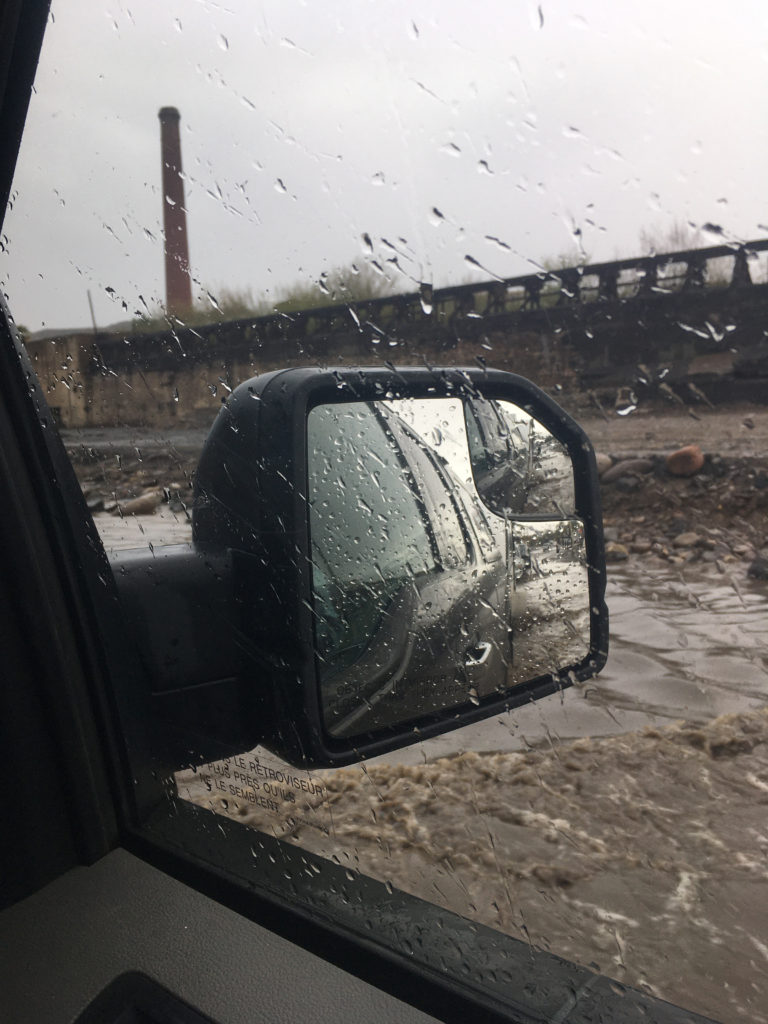 Photo taken out truck window showing muddy brown water all around and in side mirror.