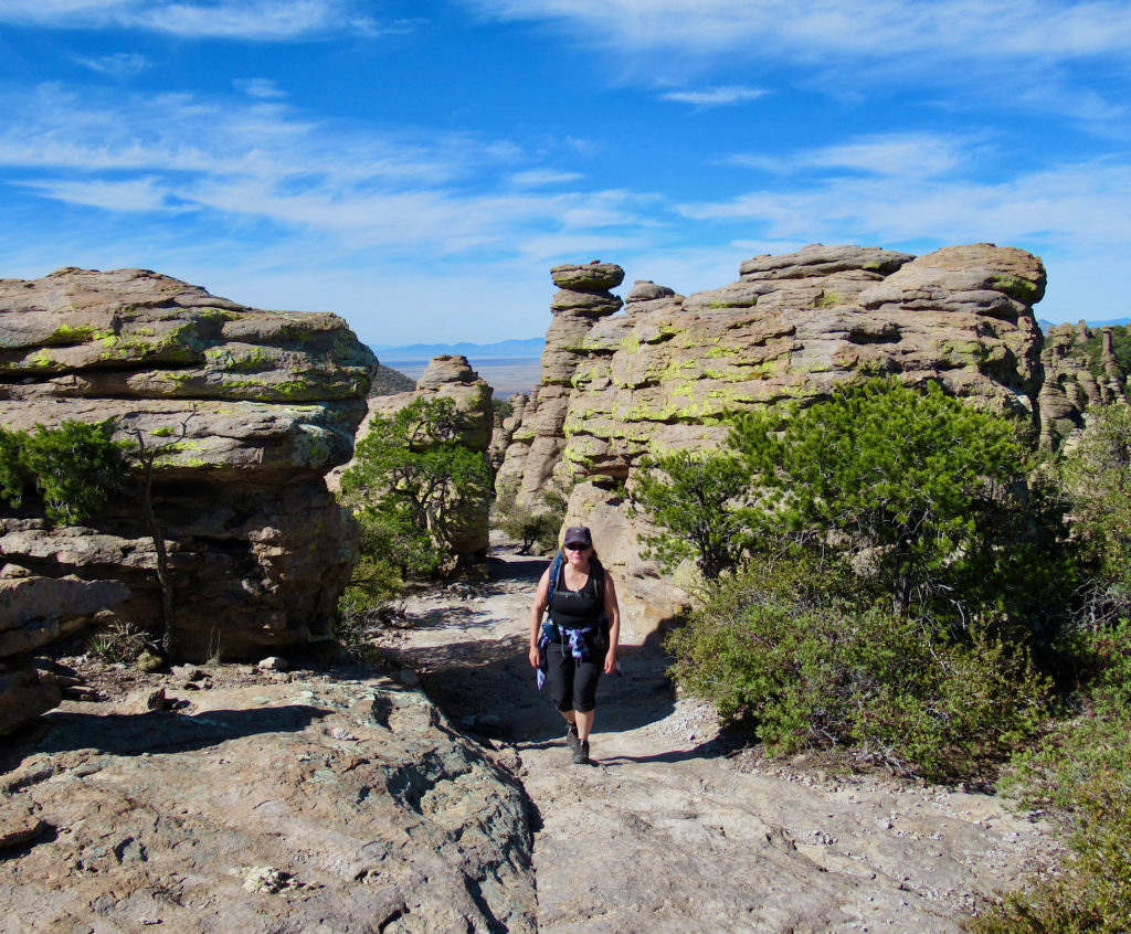 Woman hiking up path surrounded by lichen-covered rocks.