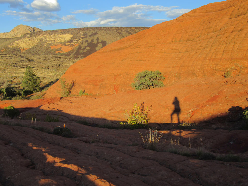 Silhouette of person with red rocks glowing in sunset above.