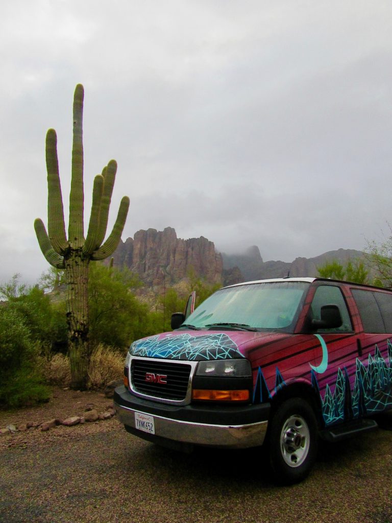 Brightly paint van in campsite with large Saguaro cactus beside it.