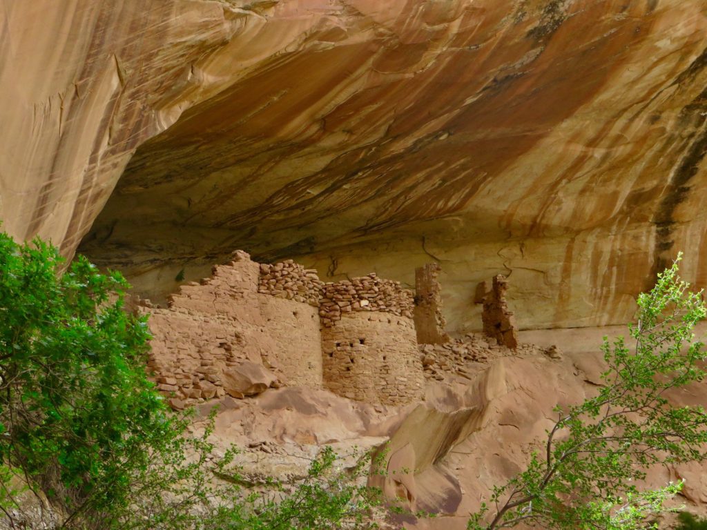 Prehistoric rock building ruin below large overhanging red sandstone alcove.
