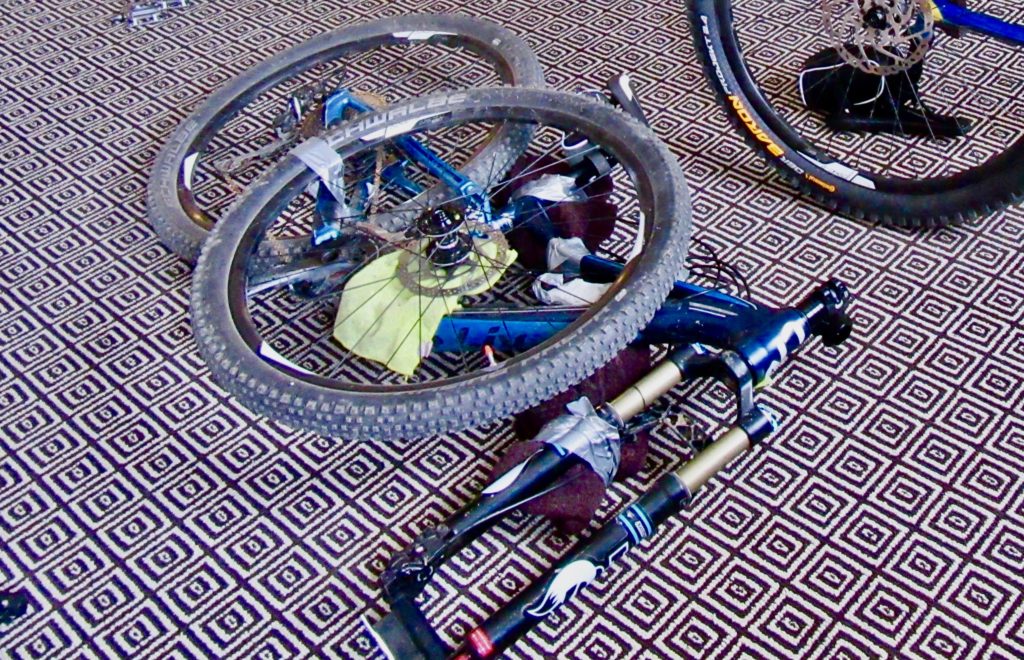 Bike laying on carpet with handlebars and pedals removed and wheels taped to frame.