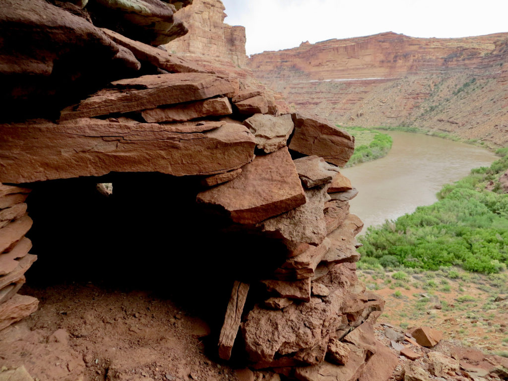 Stack stones of a structure high above muddy brown river in a canyon.