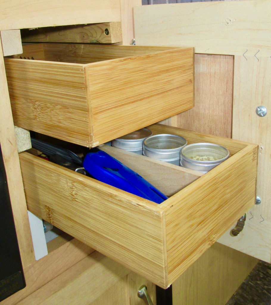 Two pulled out bamboo drawers with cutlery and round spice containers.