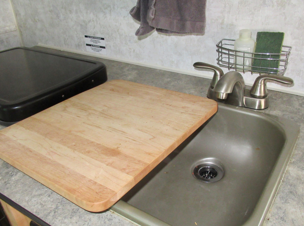 Tiny trailer counter with sink, wooden cover and metal cover for stove.