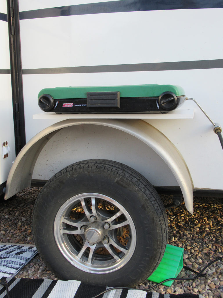 Metal trailer wheel fender with can-stove resting on shelf on top of fender.