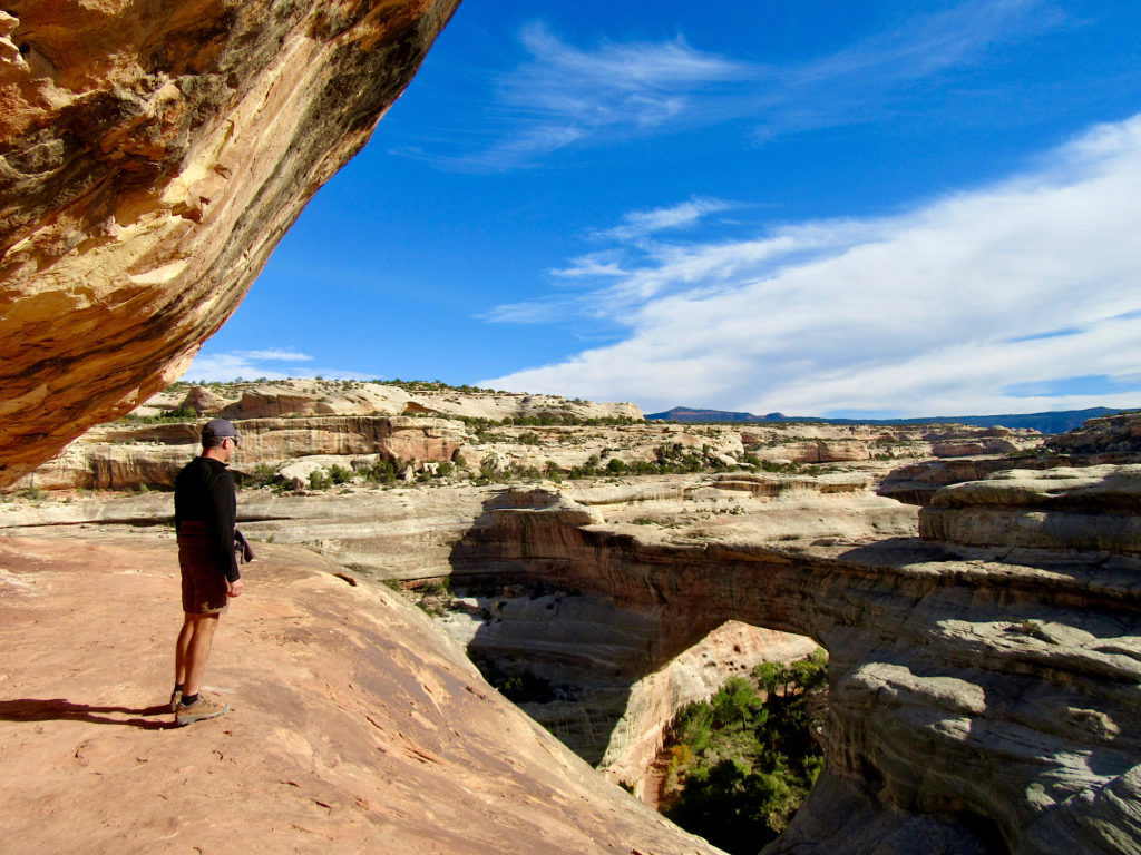 Man in short, black long-sleeved top and ball cap standing on rock ledge overlooking a canyon.