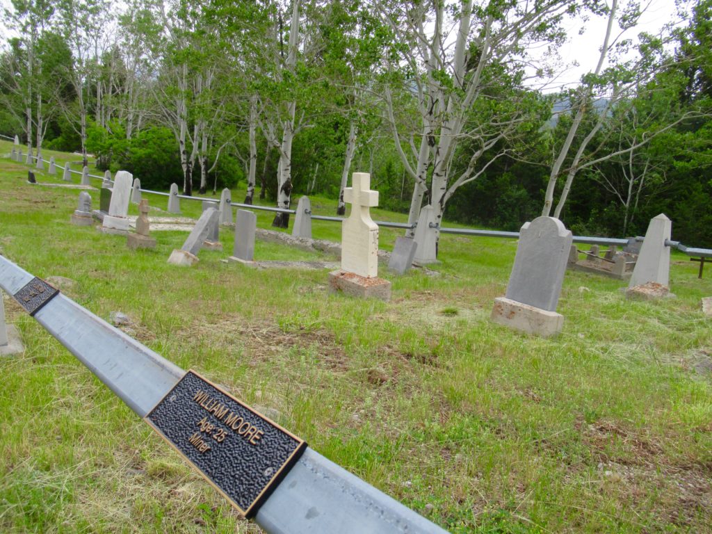 Headstone surrounded by metal rail with brass name tags of disaster victims on rail.