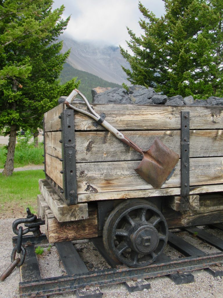 Old-fashioned wooden coal car with shovel strapped to on side.