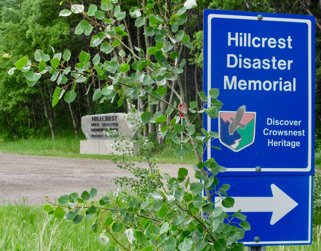 Blue street sign for Hillcrest Disaster Memorial and white arrow sign pointing to the right.