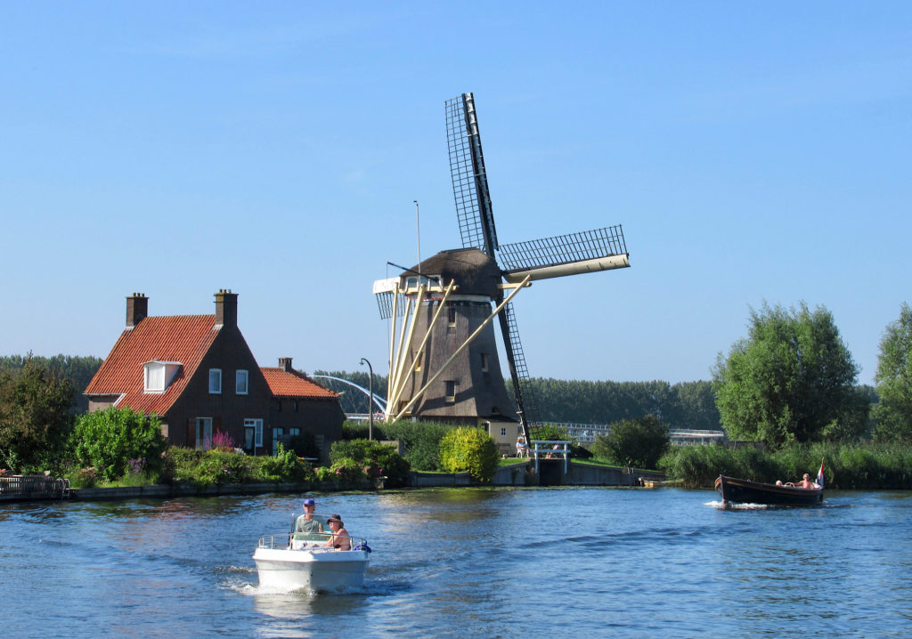 Two boats on a canal with a red-roofed house and large brown windmill on left bank.