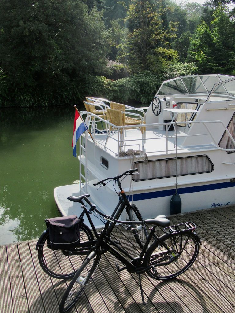 Two black bicyles on a wooden dock next to a white cabin cruiser with a Netherlands flag on back.