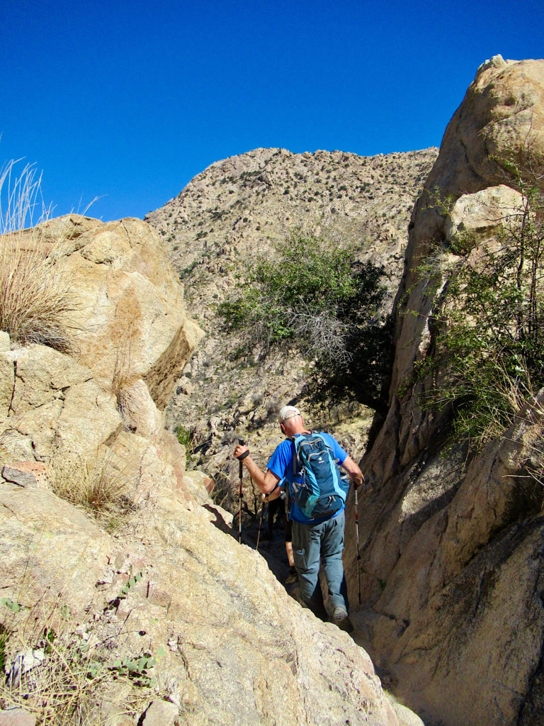 Hiker passing between two large buff-coloured sandstone rocks.
