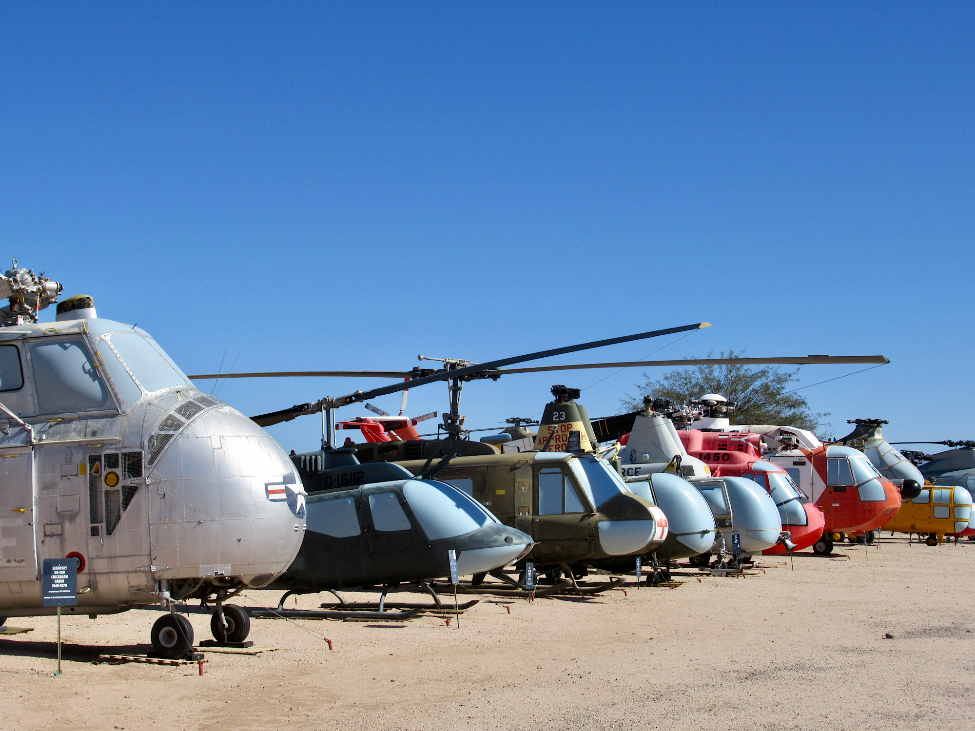 Row of multi-coloured and various-sized helicopters under blue sky.