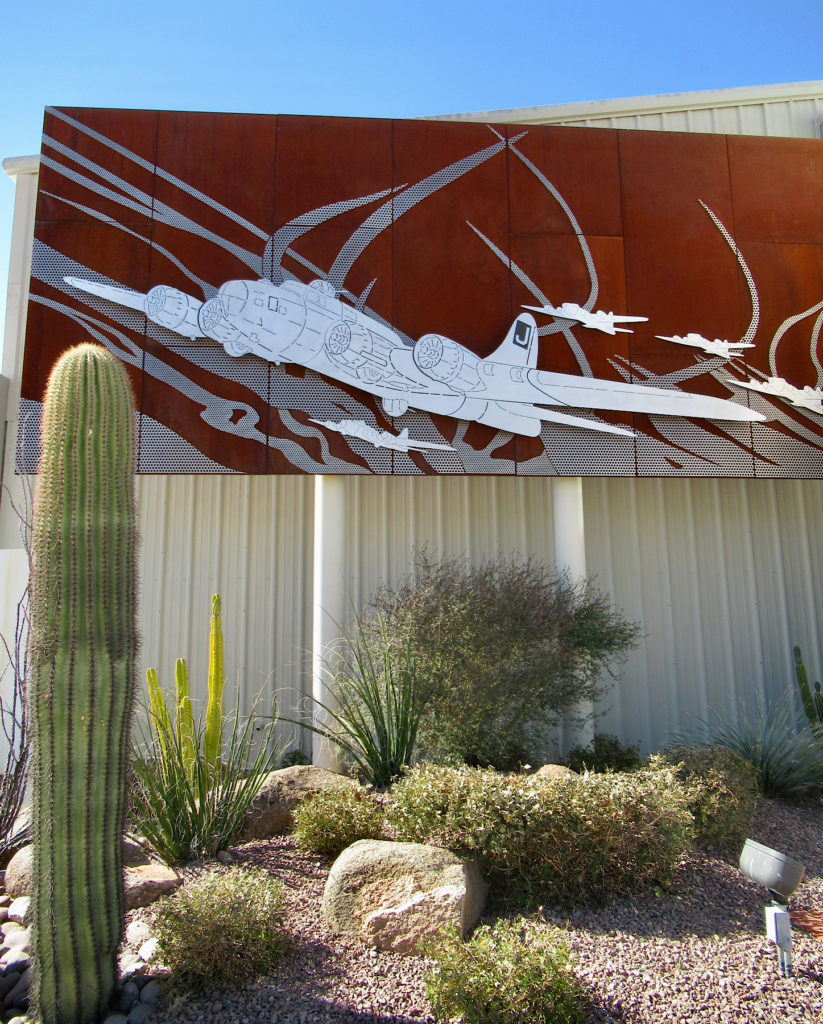 Metal art installation of B-17 bombers hanging above cactus garden on wall of metal building