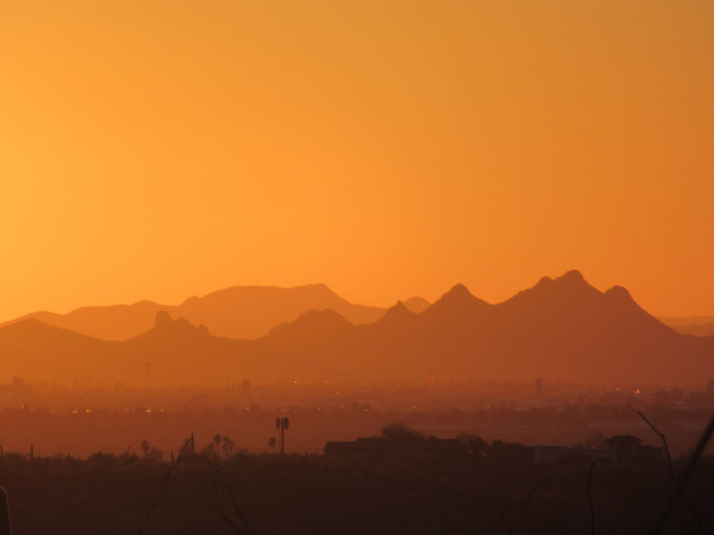 Brilliant orange sunset with a mountain range silhouetted in front.