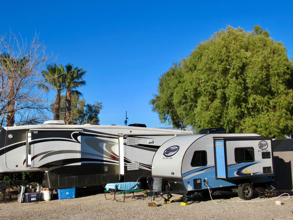 Smaller blue and white Rpod trailer next to massive, multi-slide black and white trailer in an RV Park in Tucson.