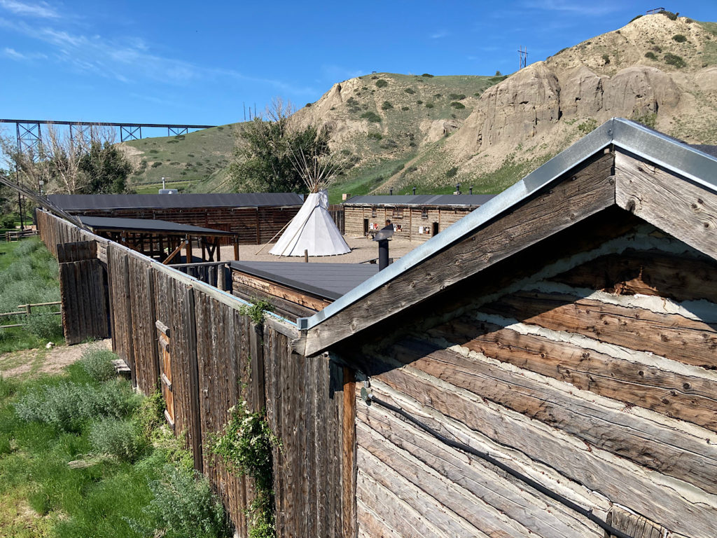 Wooden walls surrounding an inner courtyard with a large white teepee under blue sky.