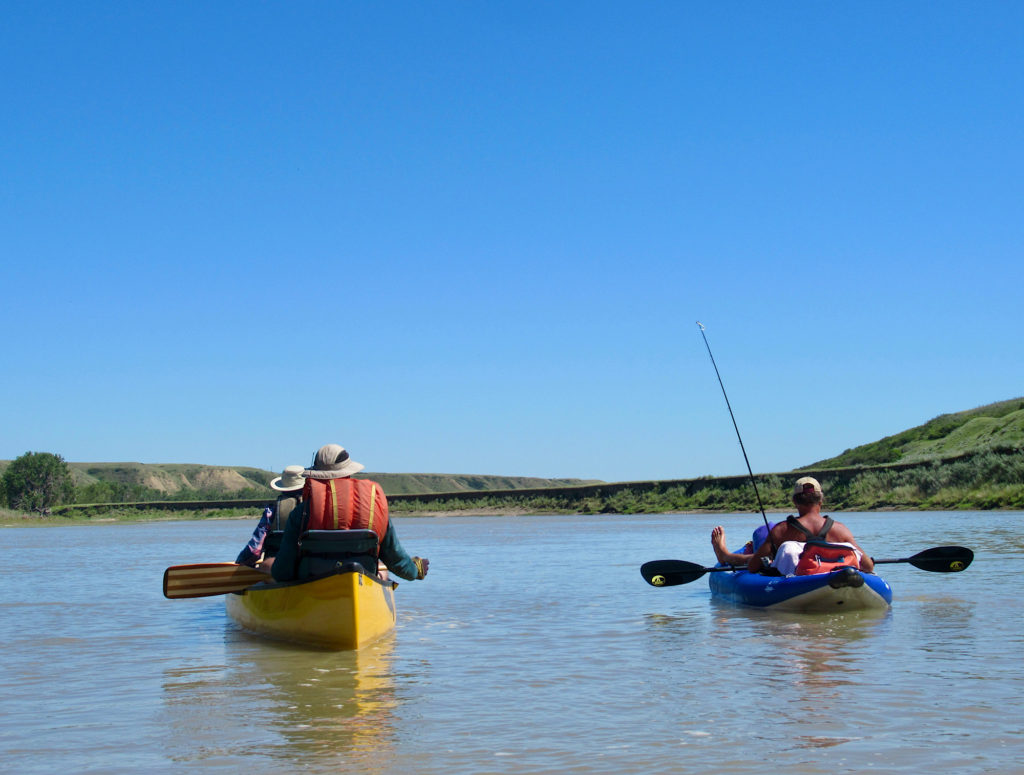 Two people in yellow canoe and one man in blue inflatable raft floating on wide river.