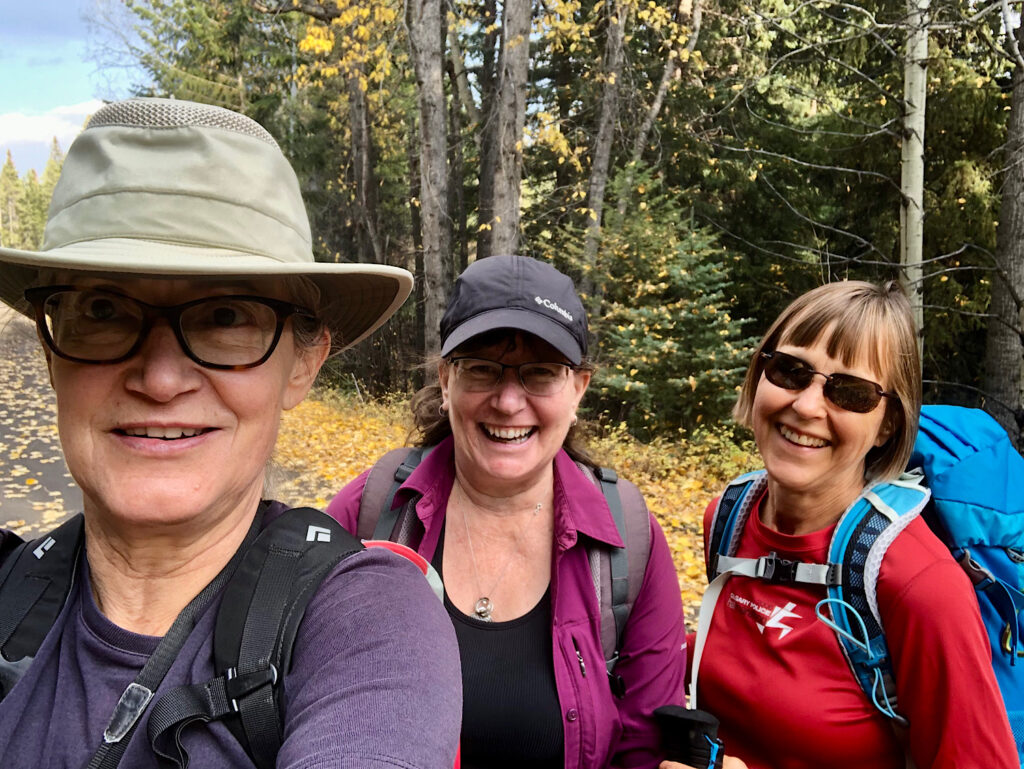 Three female hikers facing camera all smiling and wearing backpacks.