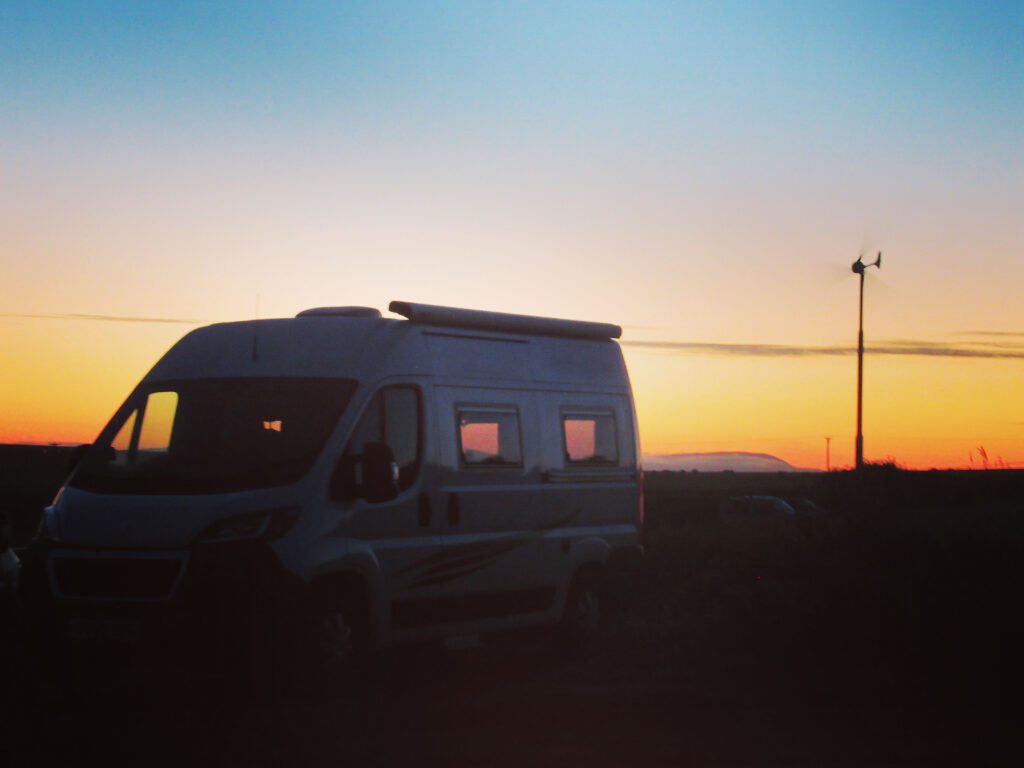 White camper van silhouetted against brilliant orange sunset.