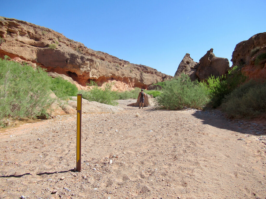 Sandy wash in desert with a signpost in middle of dry, sandy riverbed.