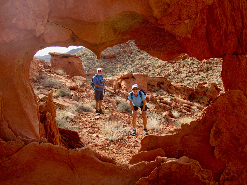 Photo taken from inside red rock cave looking out at man and woman looking back in.