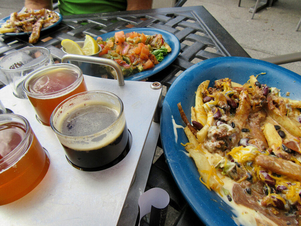 Flight of beer beside nacho fries and salsa on a metal patio table.