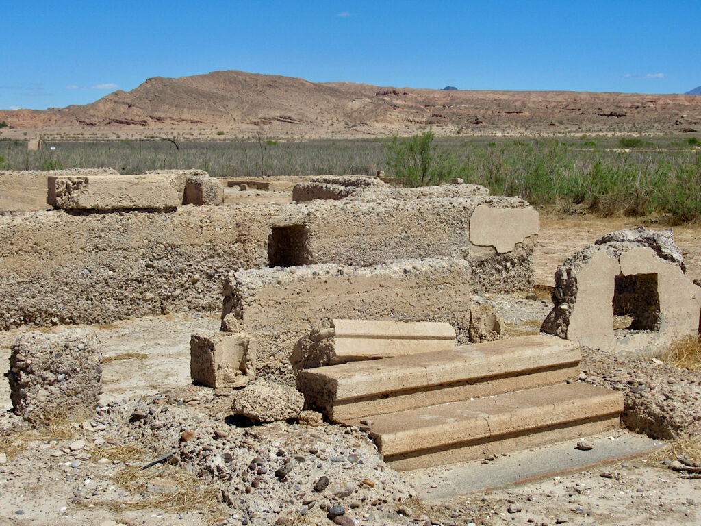 Crumbling foundation and two step staircase in a scrubby desert area with distant brown mountains.