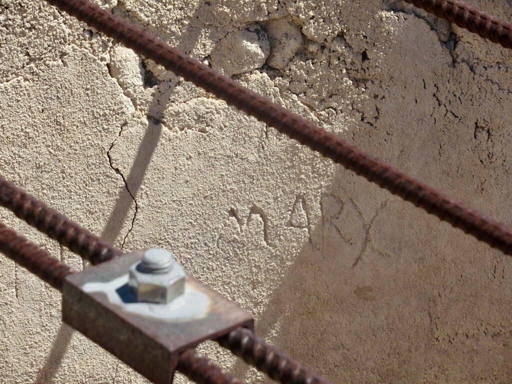 Rusted metal rebar across opening of large well with name "Mary" carved on crumbling wall.