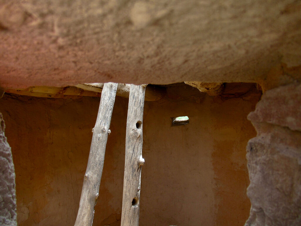 Interior of adobe building with two wood poles sticking up out of rooftop hole.