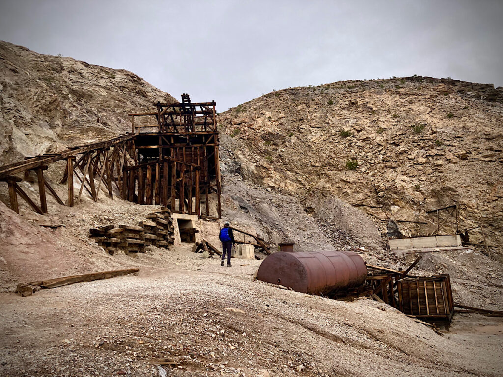 Rusting metal tanks and wooden structures at base of rocky cliff.